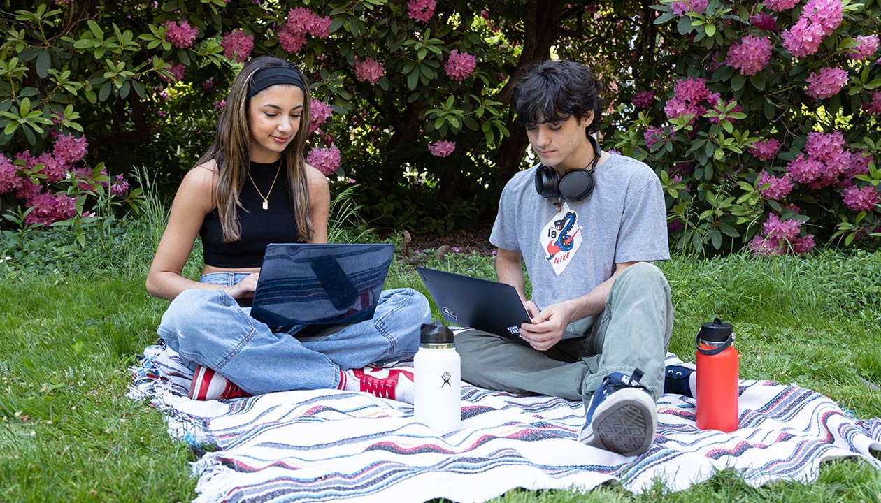 Two students study together in spring on a picnic blanket. The campus is in bloom.