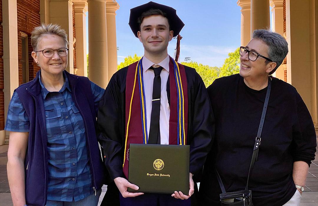 Young man in graduation gown with his two parents on either side smiling.