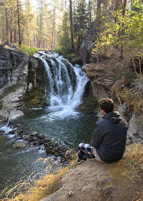 Young man looking at a waterfall in the distance.