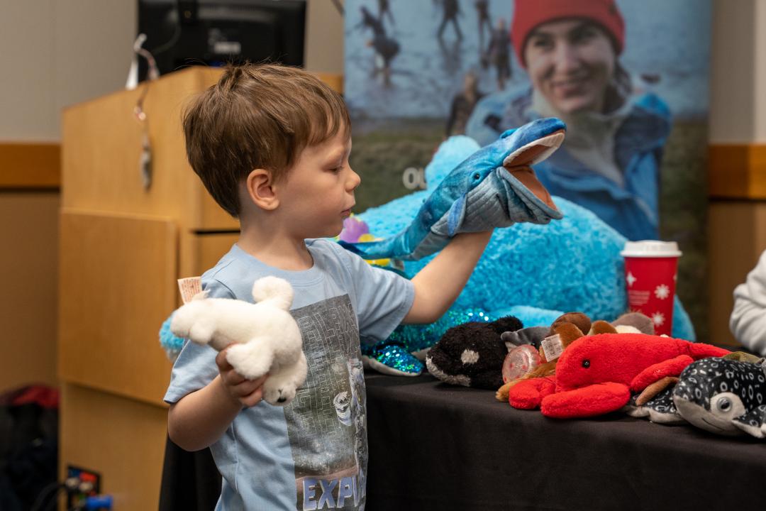 A student holds up a whale puppet in one hand and a seal in the other.
