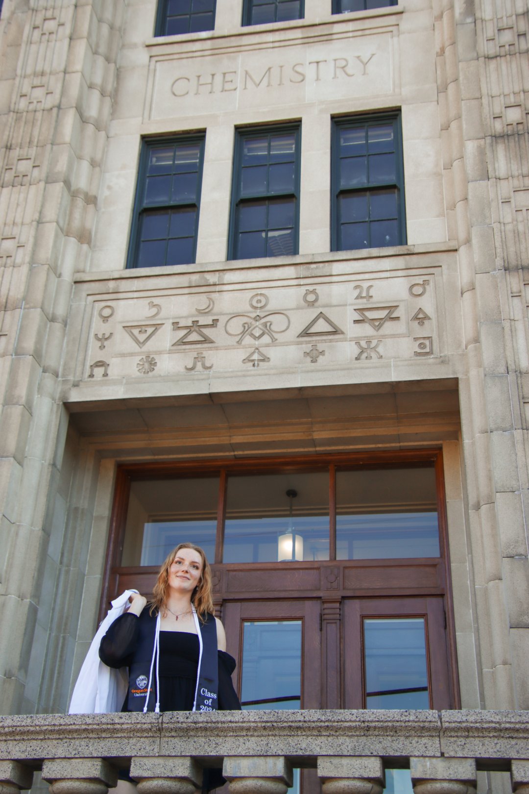 A woman stands on the Oregon State campus wearing a graduation outfit.
