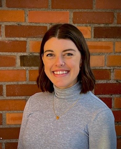 Image of Erin in front of brick wall wearing a gray shirt.