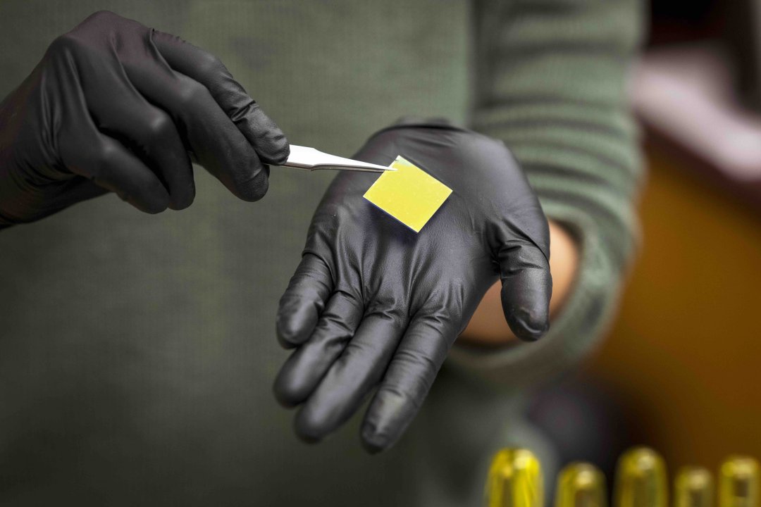 A gloved hand hold a small yellow square.