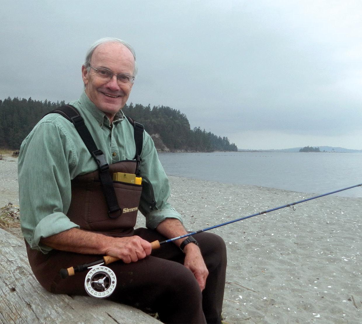 James Winton holding fishing pole sitting on log in foggy beach