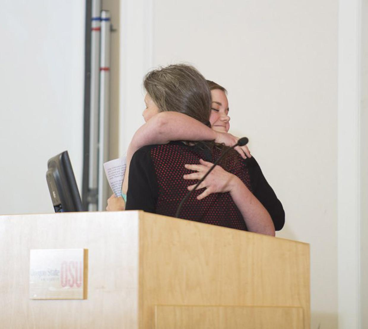 Two women hugging each other behind podium
