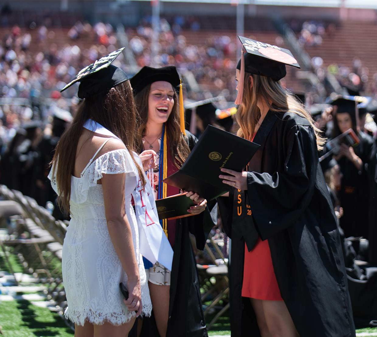 Three graduates smile together during graduation. 