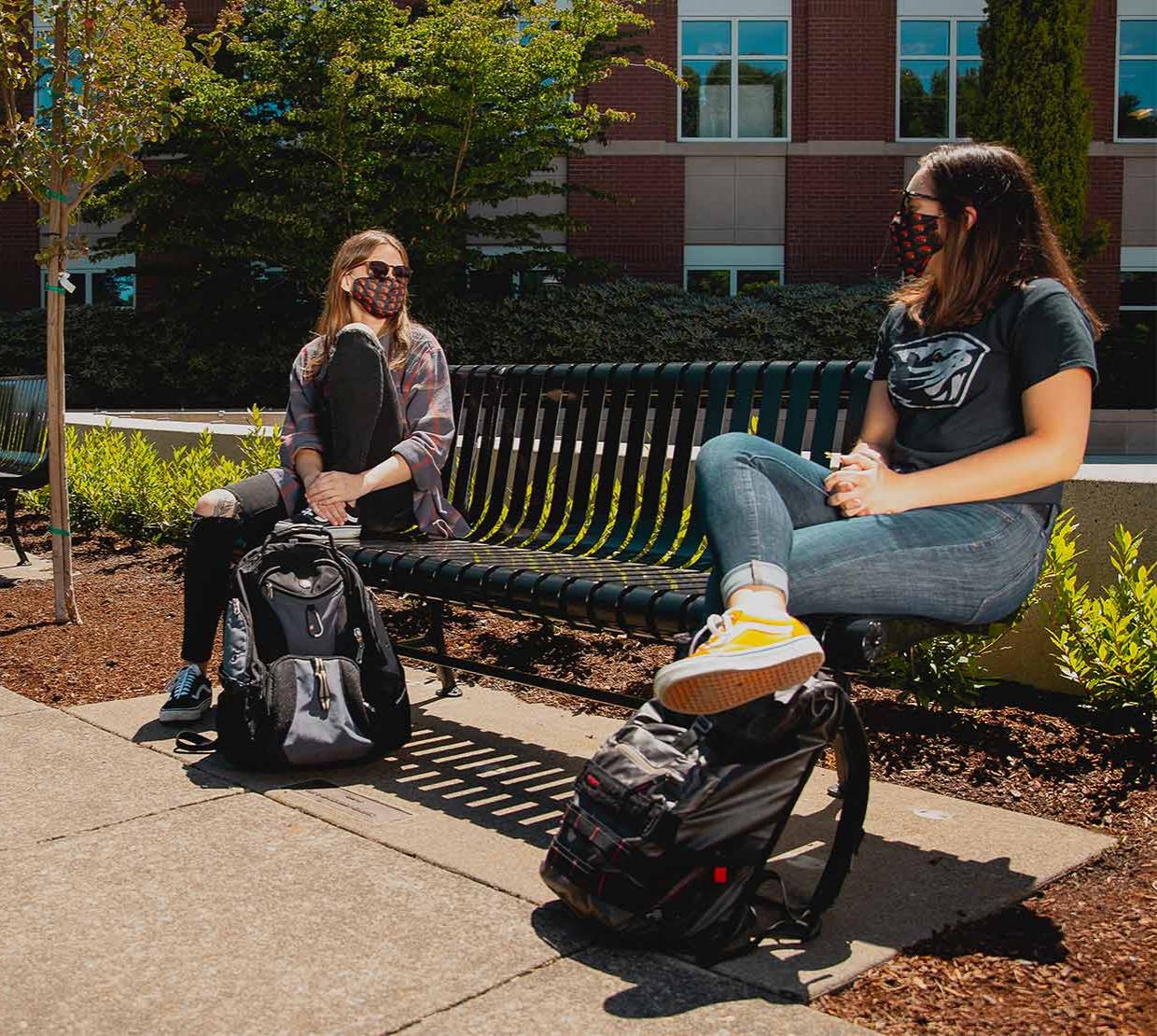 students in masks sit on a bench on OSU's campus