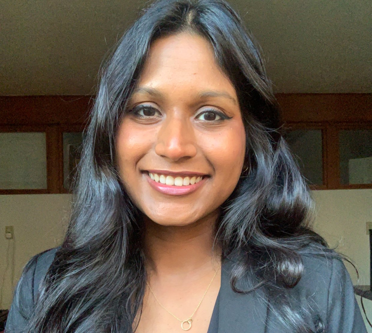 A smiling headshot of Sanjana Curtis in a blazer