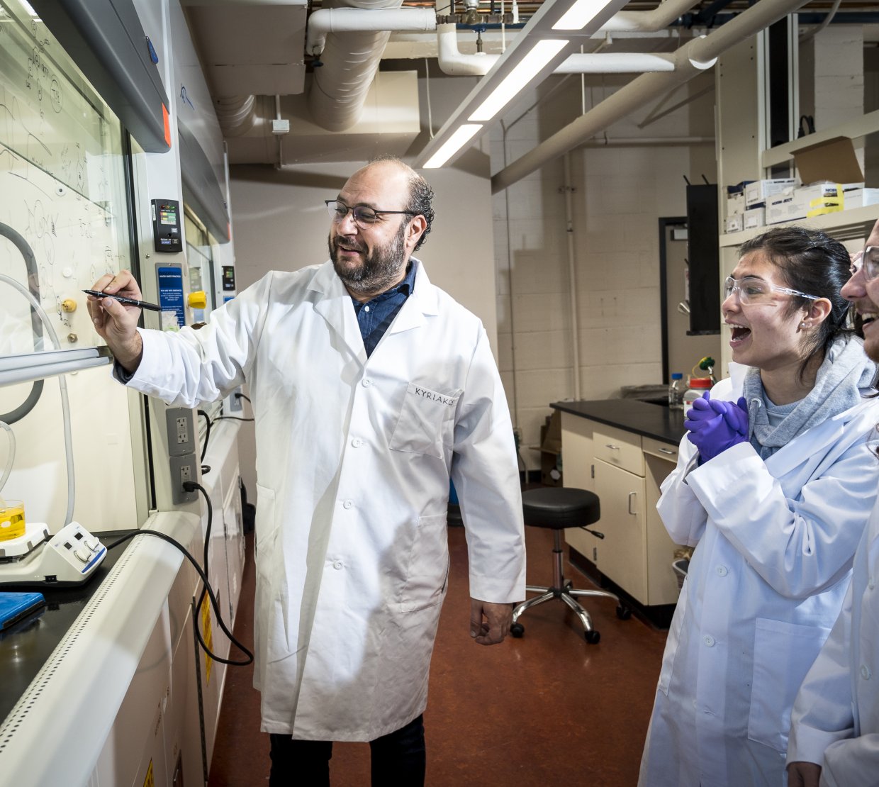 A man in a lab coat works with two students.