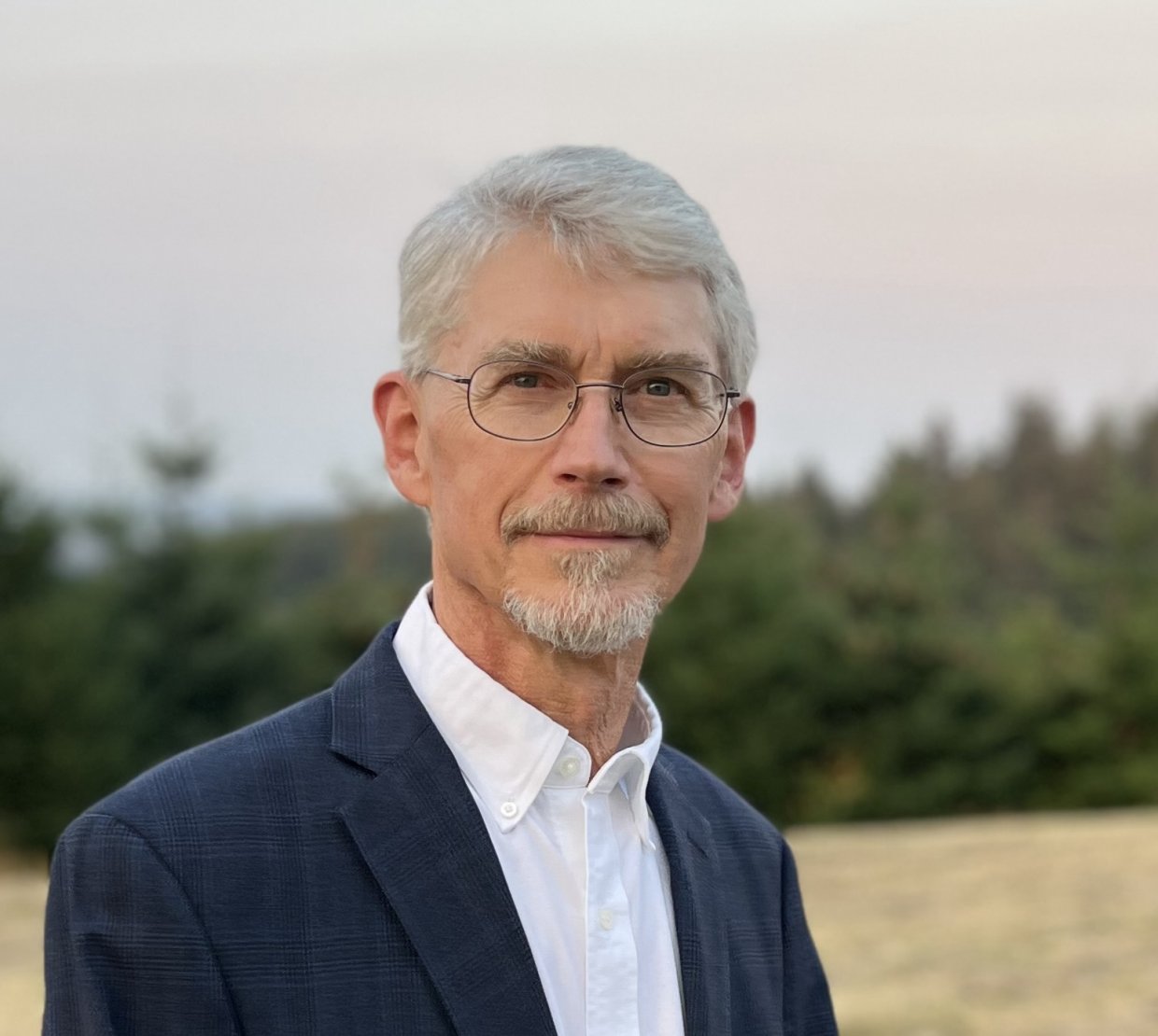 With green evergreen trees behind him, Skach smiles at the camera.