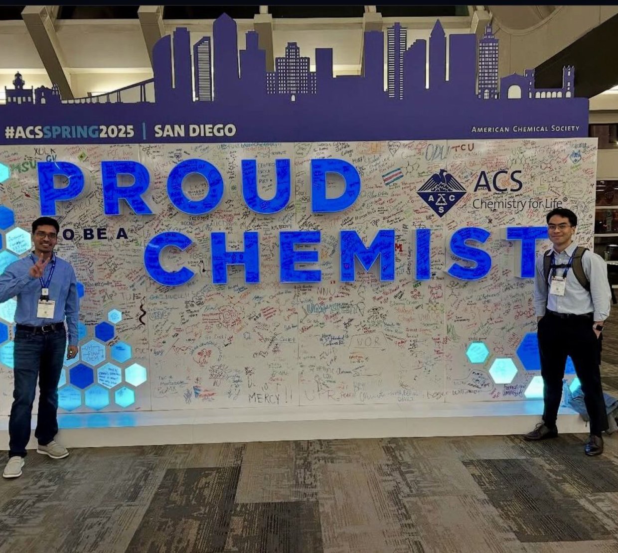 Two graduate student flank a large sign at the 2025 American Chemical Society conference that says "Proud to be a Chemist"