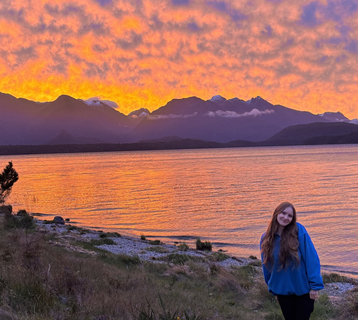 A woman stands in front of a sunset.