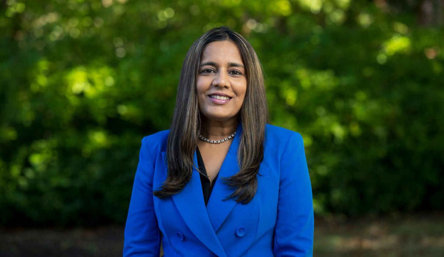 Interim Dean Vrushali Bokil stands in front of bushes on campus in a bright blue suit