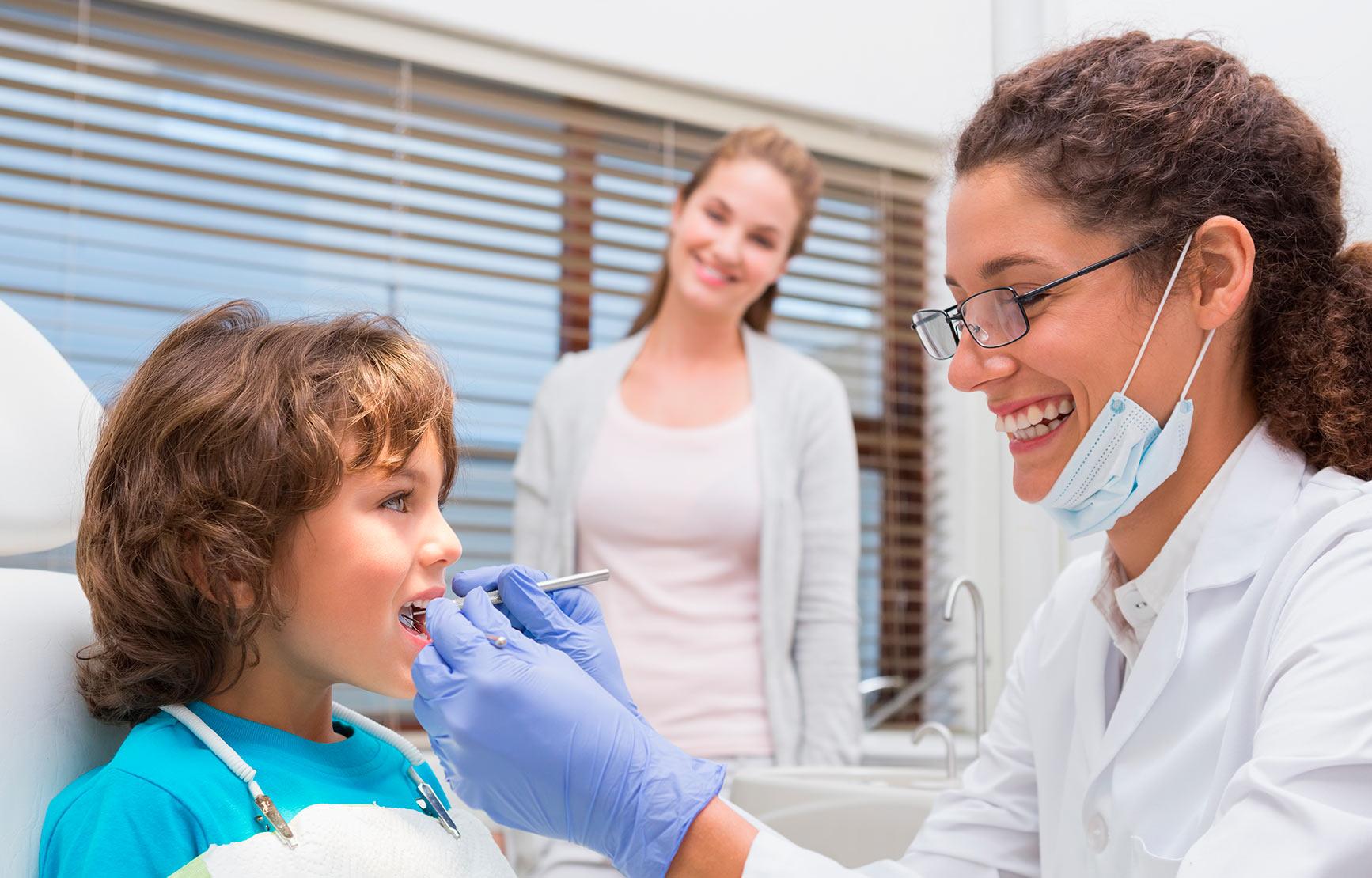 Dentist working on child's mouth next to mother