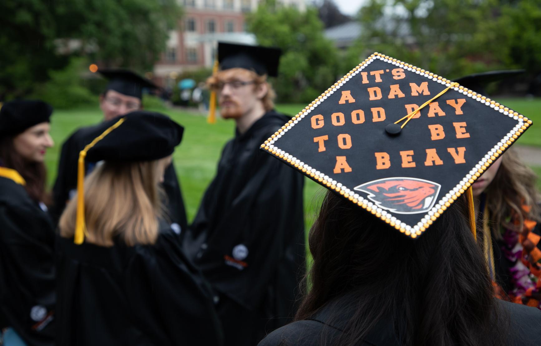 Three OSU graduates, with a grad cap that reads "It's a dam good day to be a beav."
