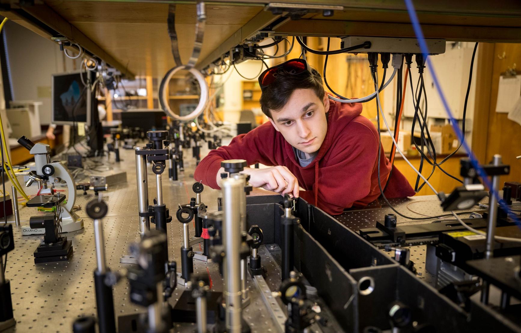 A graduate student examines the set up of an array of optics and lasers in an Oregon State University lab
