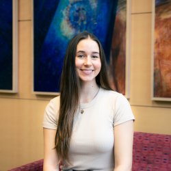 Kennedy Duff smiles for the camera in front of three colorful portraits.