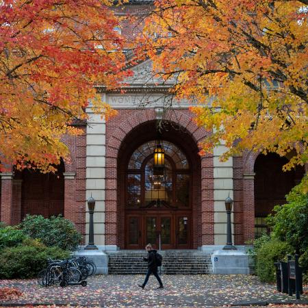 A woman walking in front of the Women's Building at OSU with fall colors