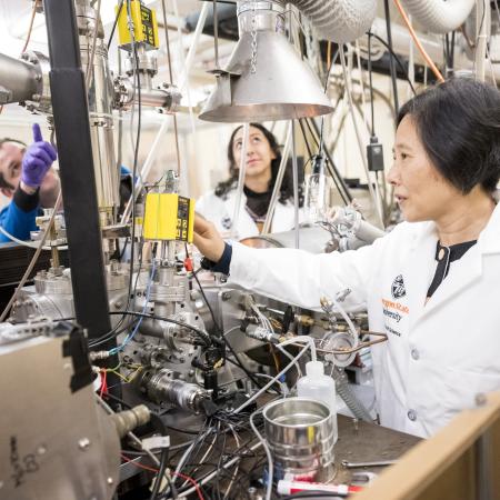 Wei Kong and graduate students work in the lab on a huge machine with wires.