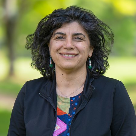 A woman in a colored print shirt and black jacket smiles for a headshot.