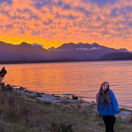 A woman stands in front of a sunset.