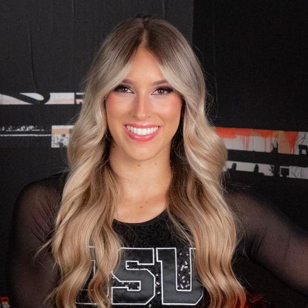 A headshot of a woman with wavy blonde hair smiling at the camera wearing a black OSU cheer uniform. 