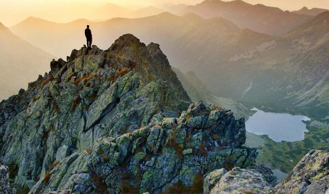 Person standing atop mountain in mountain range