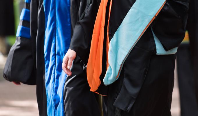 Two professors walking in doctoral gowns on campus