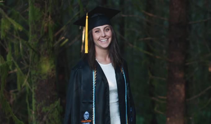 Taylor Robinson in graduation gown, standing in forest