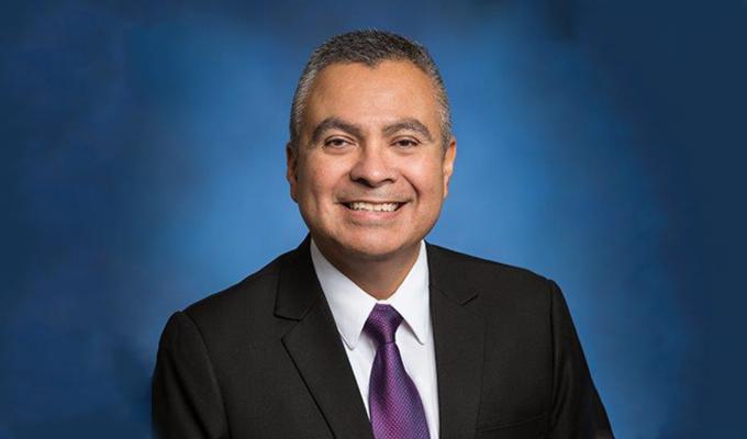 A professional photo for Roman Hernandez wearing a suit with a blue background