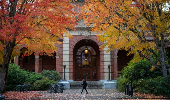A woman walking in front of the Women's Building at OSU with fall colors
