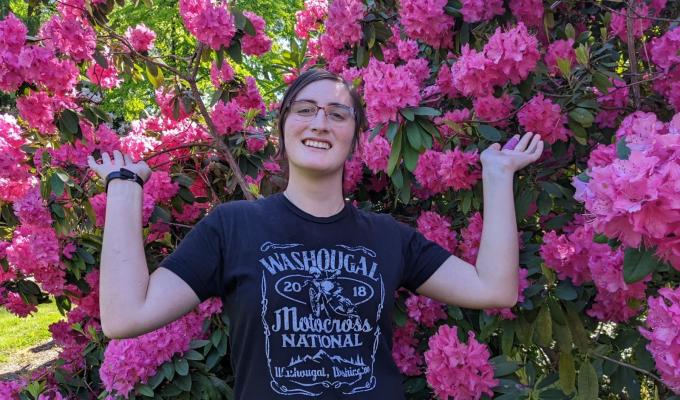 Catherine Raffin poses in front of a bush of vibrant pink flowers.