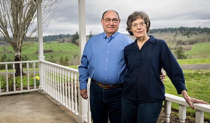 Norbert and Eileen Hartmann lean against a porch railing with green landscape behind them. 