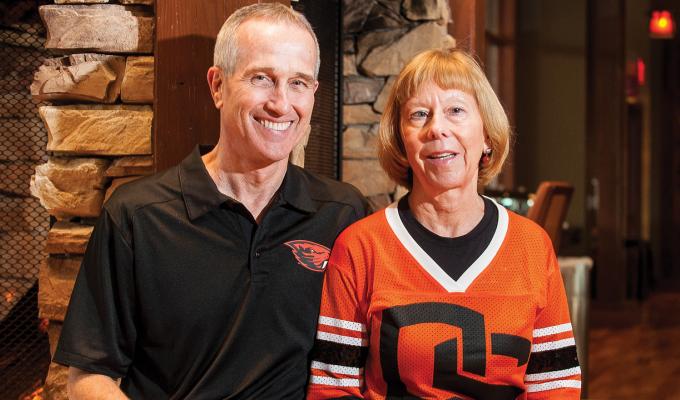 Bernard and Suzanne McGrath sit together in a home wearing Oregon State attire.