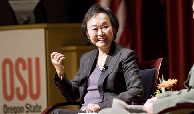 Peggy Cherng sits in a suit on stage giving a talk at an OSU event.