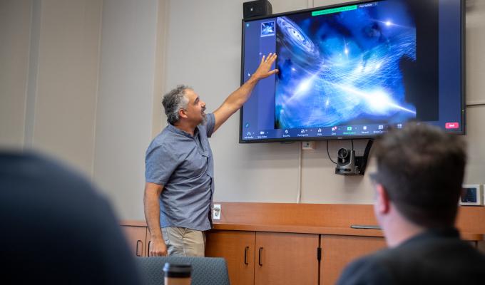 Jeff Hazboun stands in front of a computer screen on a wall looking at gravitational waves.