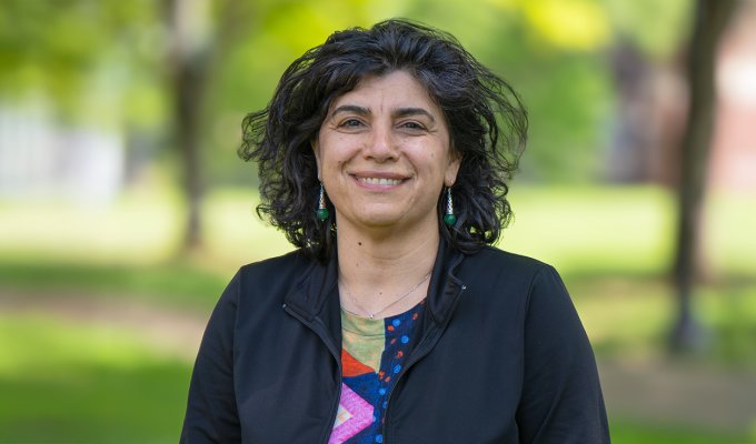 A woman in a colored print shirt and black jacket smiles for a headshot.