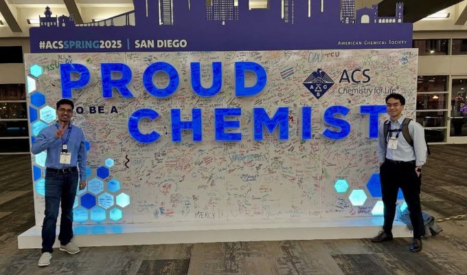 Two graduate student flank a large sign at the 2025 American Chemical Society conference that says "Proud to be a Chemist"