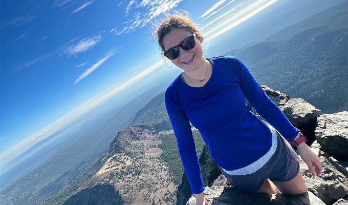 A woman in a blue shirt on top of a mountain.