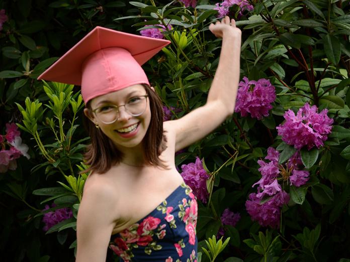 Allie Crawford standing in front of rosebush wearing pink graduation cap