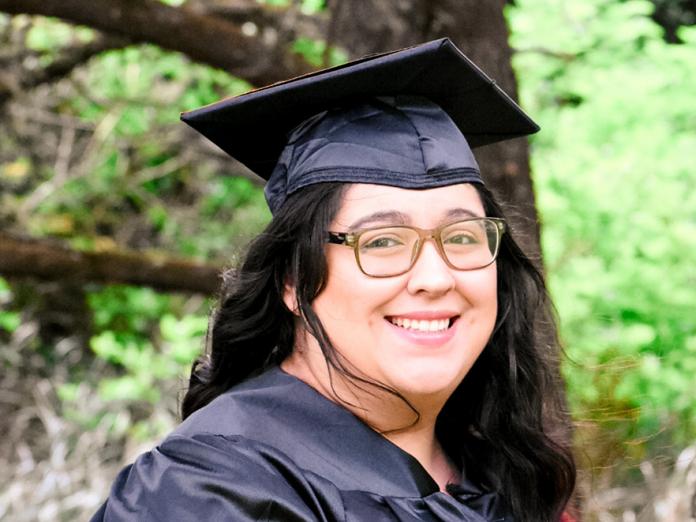 Angelica Ramirez standing in graduation gown in forest
