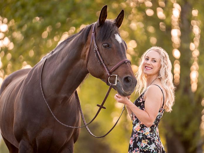 Elizabeth Cheyne standing with a horse in field.