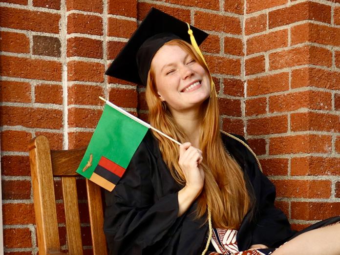 Ai Anna Richmond holding a flag and wearing her commencement cap and gown.