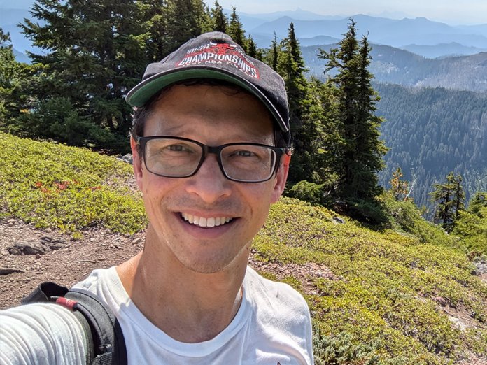 A man smiles in a scenic shot taken on a hike.