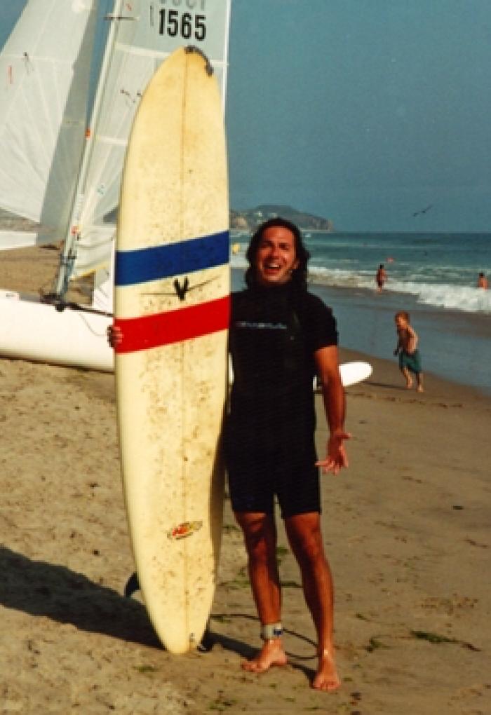 young Juan Restrepo standing on beach with surfboard