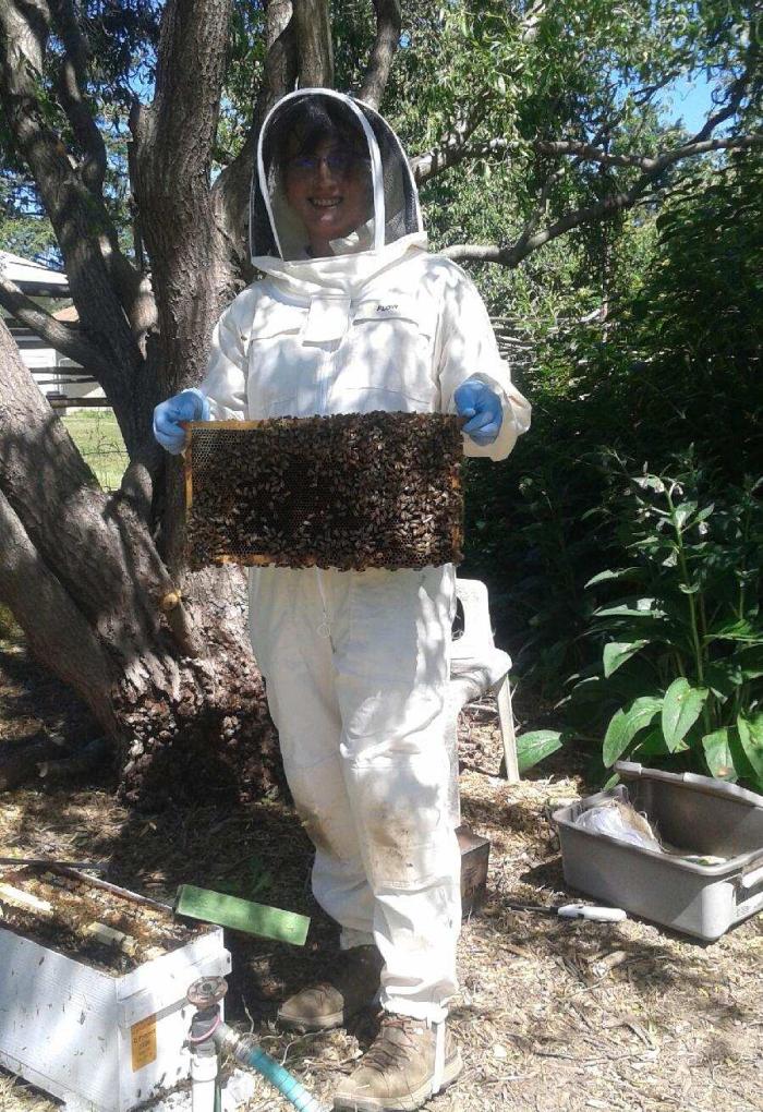 Raffin stands in a beekeeping suit holding a slat covered by a mass of bees.