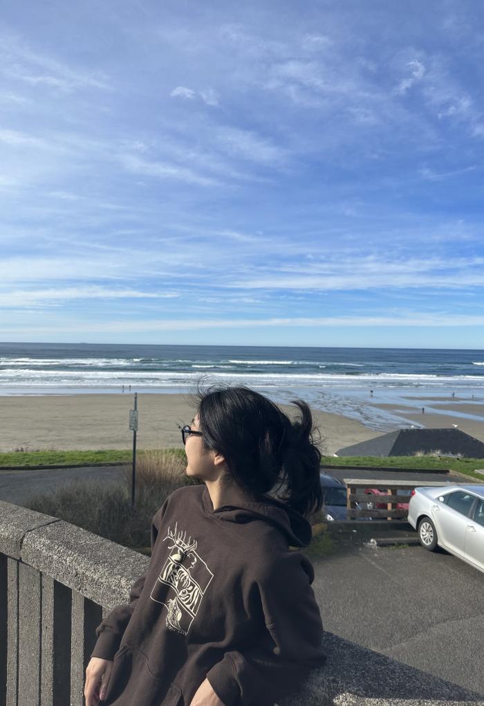 A woman leans against a concrete rail and looks out to the Pacific Ocean, wisps of clouds painting the sky.