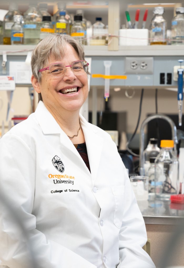 A woman in a white lab coat sits on a stool in a laboratory.
