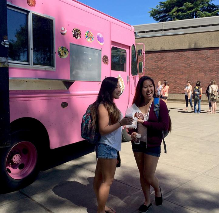 female students grabbing donut from pink delivery truck