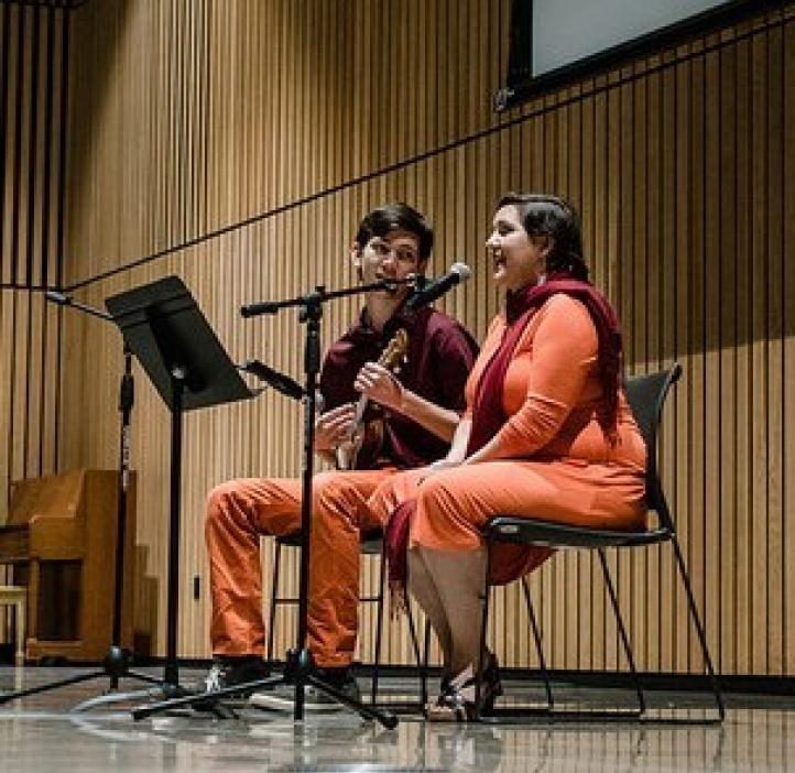 two students singing and playing ukulele on stage